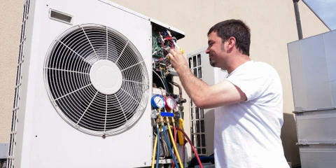 Un homme en t-shirt rayé effectue la maintenance d'un climatiseur mural split dans un bureau aux murs blancs et plafond suspendu