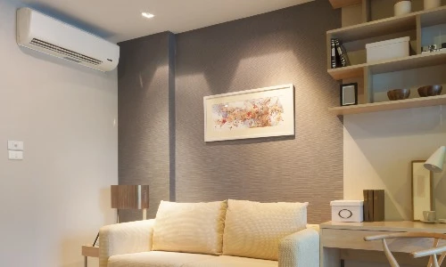 Homme d'affaires en chemise beige utilisant une télécommande pour contrôler un climatiseur mural dans un bureau moderne avec baies vitrées