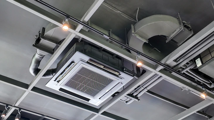 Plafond technique industriel avec système de climatisation cassette encastré, conduits de ventilation métalliques apparents et éclairage sur rails