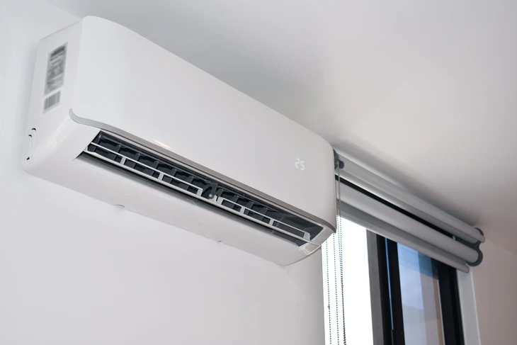 Intérieur moderne avec climatiseur mural blanc installé près d'une fenêtre avec store vénitien