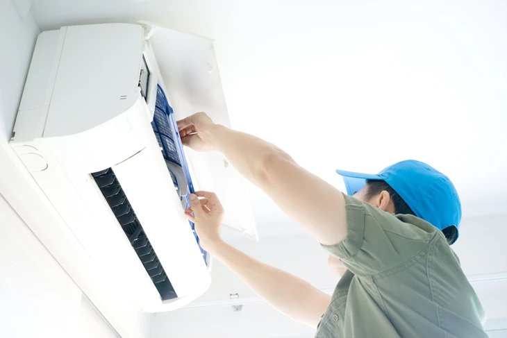 Technicien en casque bleu installant ou réparant une unité de climatisation murale intérieure dans un environnement résidentiel