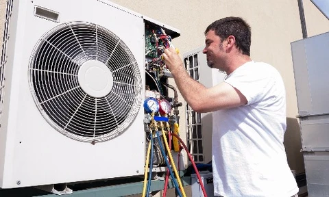 Unité extérieure de climatisation blanche montée sur support métallique fixé au mur en briques rouges d'un bâtiment
