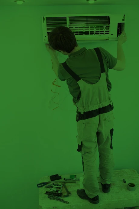 Technicien en combinaison de travail effectuant la maintenance d'une unité de climatisation murale dans un environnement intérieur
