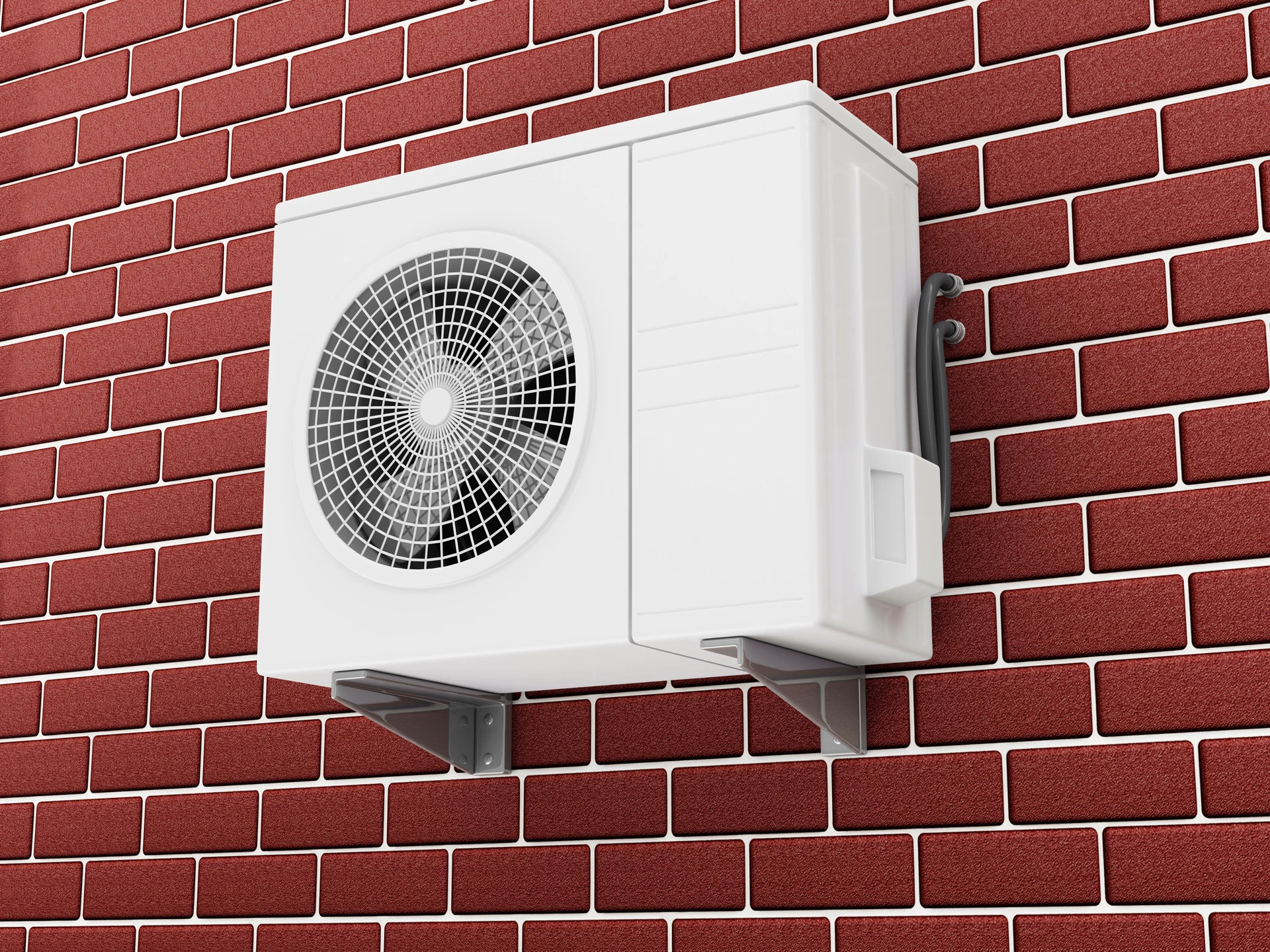 Unité extérieure de climatisation blanche montée sur support métallique fixé au mur en briques rouges d'un bâtiment