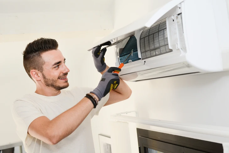 Technicien souriant effectuant la maintenance d'une climatisation murale split dans un intérieur résidentiel moderne