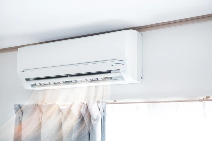Intérieur résidentiel avec climatiseur mural blanc monté au plafond en fonctionnement, diffusant de l'air frais visible par effet de brume
