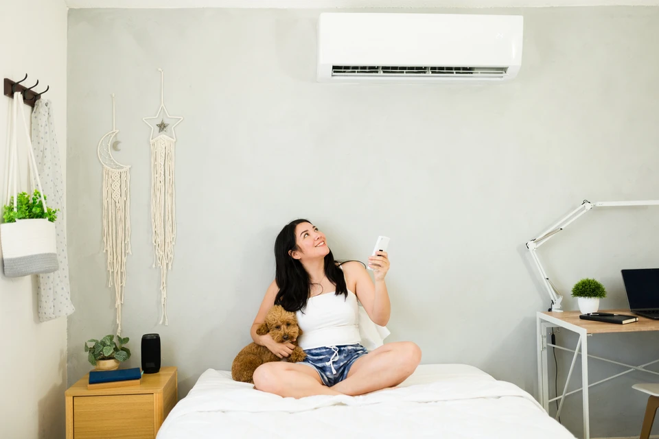 Une femme souriante avec télécommande profite de la brise rafraîchissante d'un mini-système de climatisation à deux vitesses par une chaude journée d'été