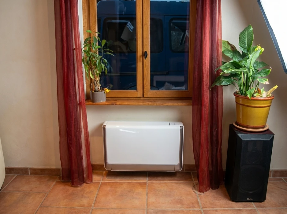 Intérieur résidentiel avec climatiseur console mural blanc posé au sol sous une fenêtre à volets en bois