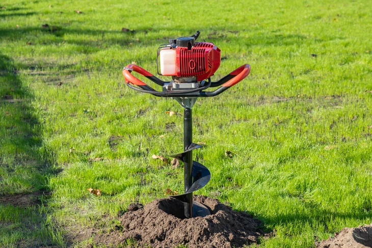 Scène extérieure sur pelouse verte avec tarière thermique en fonctionnement