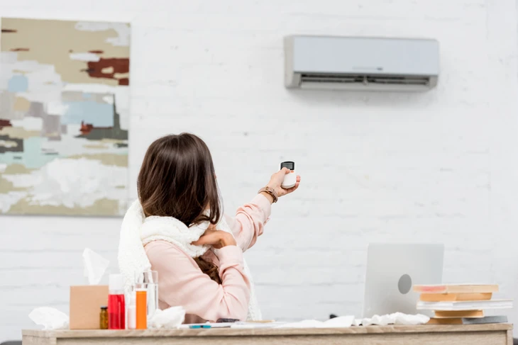 Femme en peignoir rose utilisant une télécommande pour contrôler un climatiseur mural dans un intérieur moderne