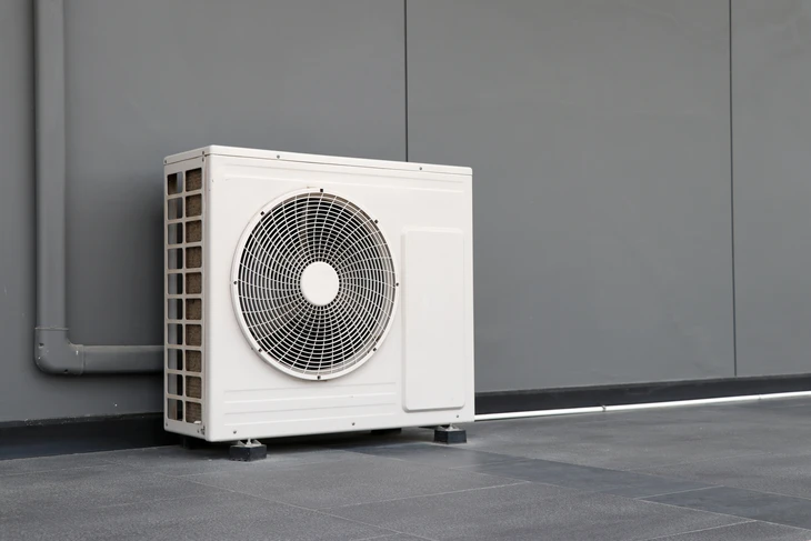 Unité extérieure de climatisation installée sur terrasse extérieure contre mur gris