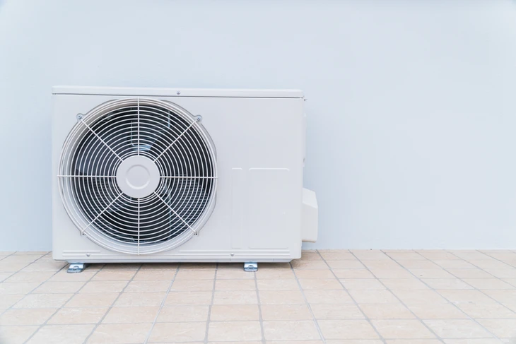 Extérieur résidentiel avec unité de climatisation posée sur carrelage beige contre mur blanc