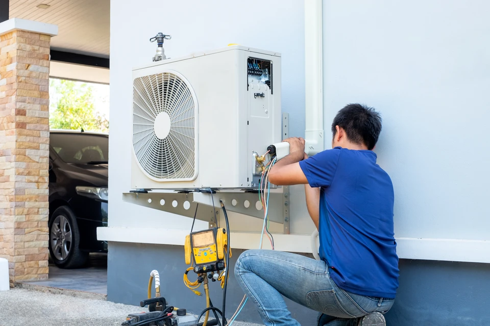 Technicien en climatisation travaillant sur une unité extérieure de pompe à chaleur installée sur terrasse résidentielle