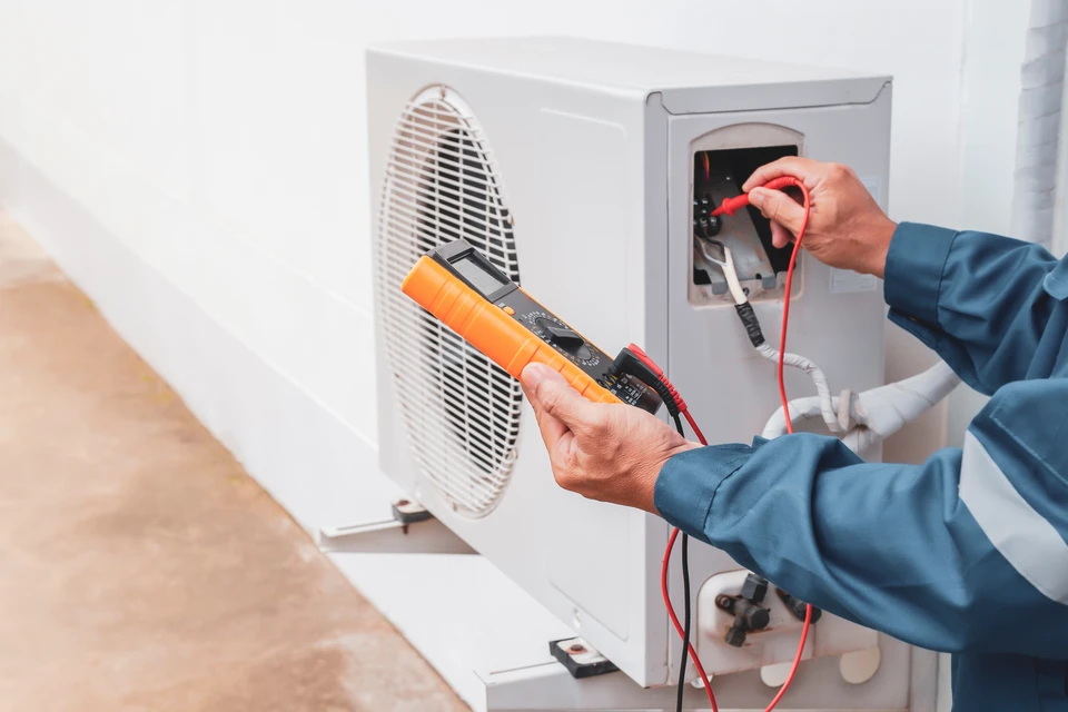 Technicien en climatisation travaillant sur un toit, agenouillé près d'unités de climatisation extérieures, utilisant un ordinateur portable pour diagnostic ou maintenance
