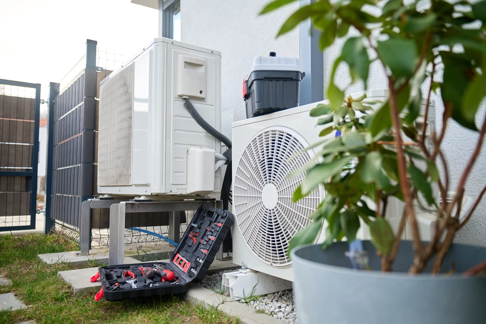 Technicien en climatisation tenant des manomètres à l'extérieur devant une unité de climatisation résidentielle